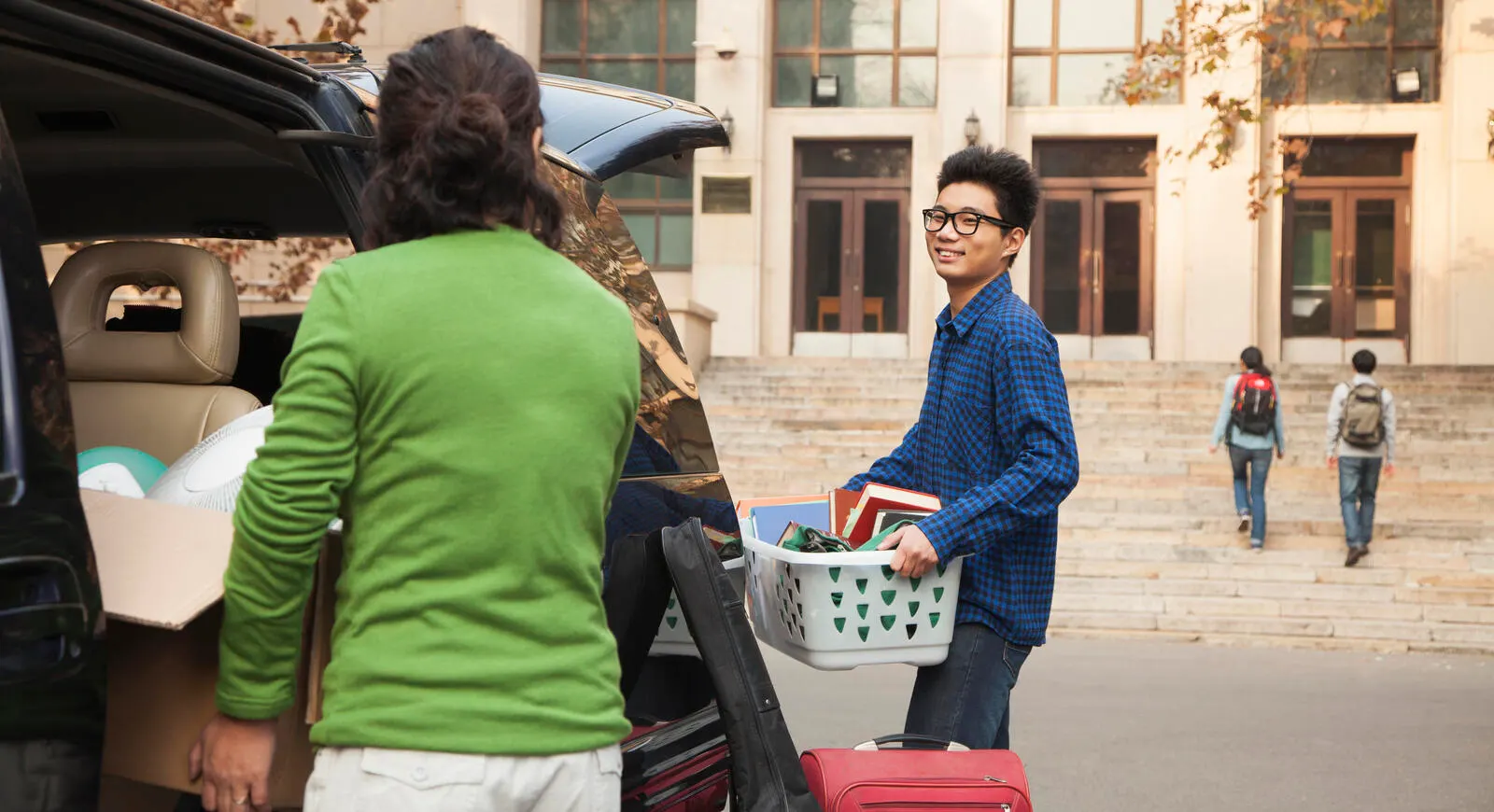 Mother with college aged son unpacking the car in front of the dorm.